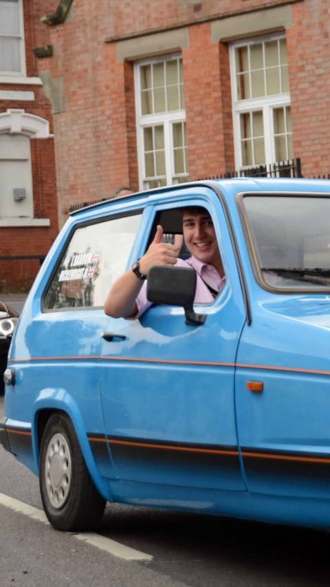 Person smiling and giving a thumbs‑up while sitting in a blue vintage car.