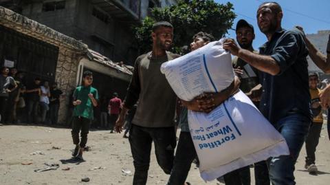 nternally displaced Palestinians carry bags of flour near a food distribution point in Zikim, northern Gaza Strip, 27 July 2025. T
