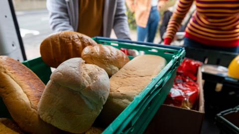 A generic photograph of volunteers unloading fresh food in a container from the back of a van 