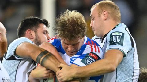 Stormers number eight Evan Roos is tackled by two Ospreys defenders