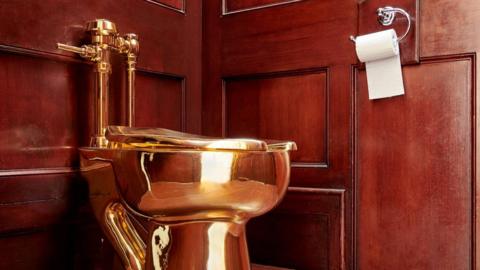 A picture of a gold toilet inside a small brown wood pannelled room. 