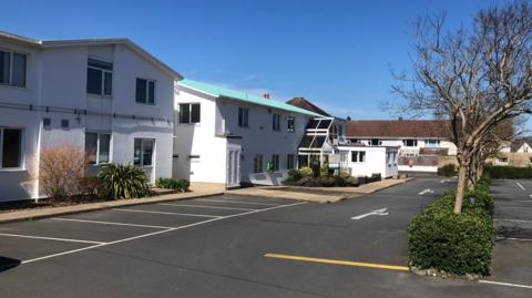 Raymond Falla House - A large car park in front of a white building with a green roof.
