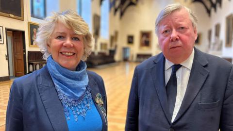 Head and shoulders picture of Lord Justice Clerk Lady Dorrian and Lord President Lord Carloway. They are standing side by side in grand looking room. Both are smiling at the camera. Lady Dorrian has short blonde/grey hair and is wearing a navy blazer with blue scarf. Lord Carloway has swept over grey hair and is wearing a nazy suit jacket, white shirt and black tie.