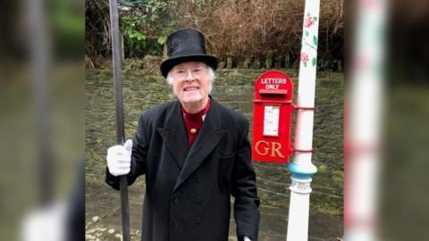 Reg Ling stood next to Frome's Valentine's lamp. He is wearing a long black formal jacket and a black top hat and white gloves