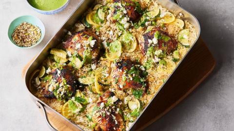 A traybake with golden chicken thighs baked over rice with courgette and lemon slices.