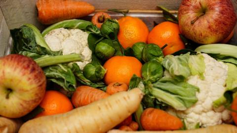A picture of vegetables and fruit. There is items including oranges and apples. They are all piled on top of one another.