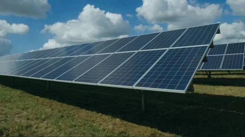 A close up of a line of solar panels positioned on grass. 