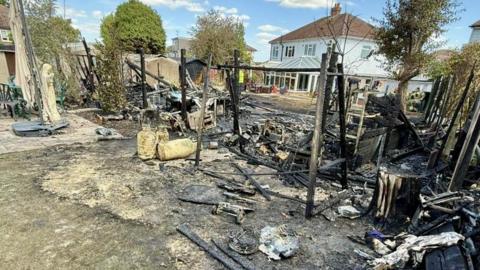 Photo of where a fire had happened in a garden. There is burnt wood on the floor and a small wooden structure in the middle of the image.
