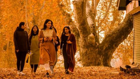 Kashmiri girls walk amongst the autumn foliage under chinar trees, which have changed colour in the Nishat Mughal garden, on November 11, 2020 in Srinagar, the summer capital of Indian-administered Kashmir, India.