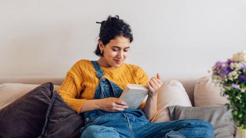 Woman reads a book on the sofa.