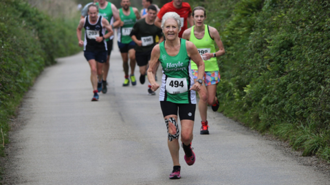 A woman, Andrea Simmons, running along a road in a green running vest
