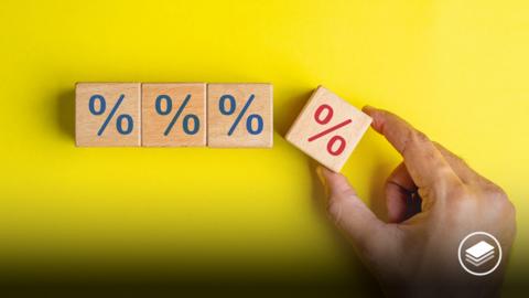 A hand holding a wooden block with a red percentage on, with three other wooden blocks on with blue percentage sign on.