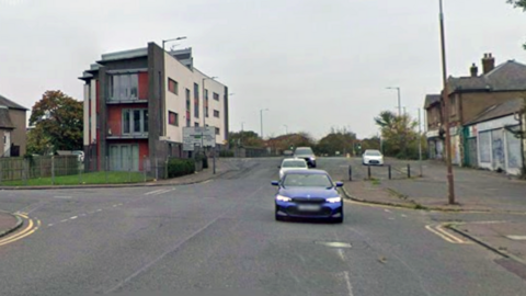 Road with cars on it and flats, houses and shops on either side