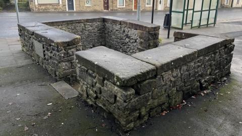 An ancient well made up of four brick walls with gaps at either end