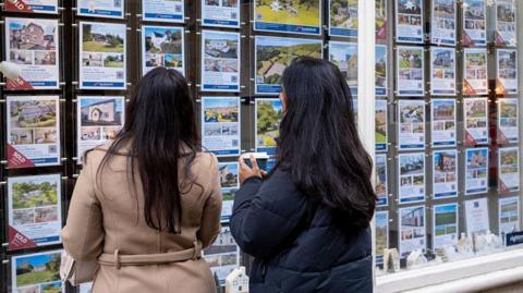 Two women looking at property details in an estate agent's window