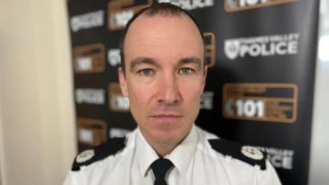 Surrey Police Chief Constable Tim De Meyer wearing a white shirt with black shoulder pads and a black tie.