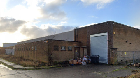 A screengrab of a large brick building with grey shutters.