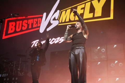 Charlie Simpson and Matt Willis from busted stood in front of a screen that reads "Busted VS McFly Tour 2025"