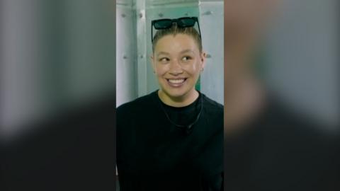 A woman smailes. She is wearing a black t shirt and has sunglasses on her head