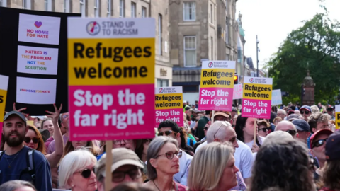 Crowd of people holding placards saying "Refugees welcome: stop the far right".