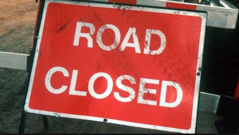 A battered red sign with road closed in white lettering