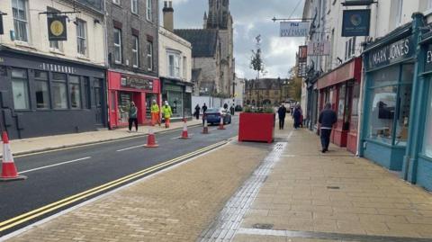 Fisherton Street with a widened pavement, shops and Salisbury Cathedral in the background