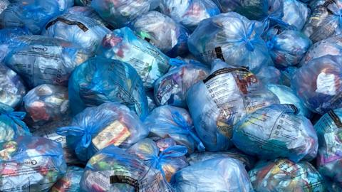 Blue bags of waste lie in a pile at a recycling centre.