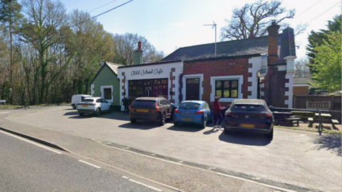 Four vehicles parked outside a single-floor building. The building is split into three colours - green on the left, white in the middle and red on the right. The image is taken from in the road outside the building.