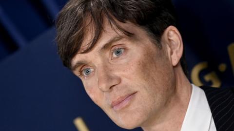 Cillian Murphy looking to the left, he is wearing a white shirt and black jacket