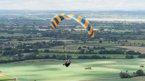 A paraglider flies over English countryside.