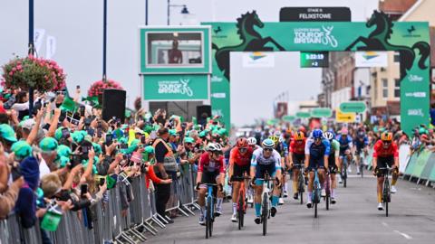 The Tour of Britain race finishing in Felixstowe in 2024. Bike riders race down a road with spectators cheering them on from either side of the road.