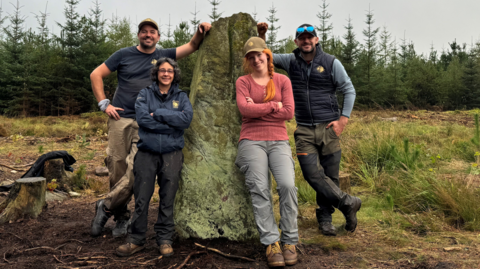 Time team stood leaning on Farley Moor standing stone