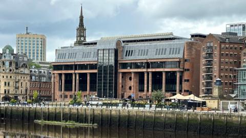 An imposing court buidling made from smooth red-tinged stone and columns, with large dark windows.