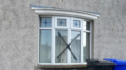 Bay window on a pebble-dashed house that has an X across two of the four panes. 