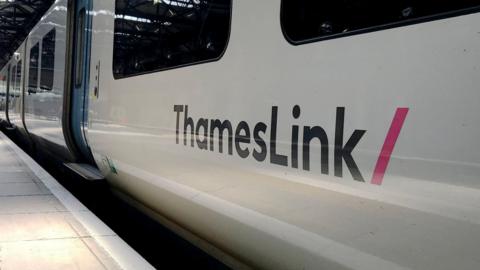 A white Thameslink train parked at a station. It has the company name on its side in navy font.