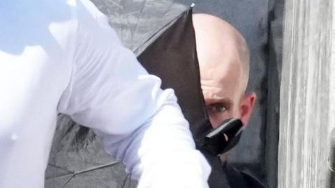 A close-up image of Jake Mullarkey outside court, partially hidden behind a black umbrella.