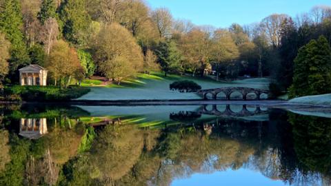 A perfect mirror image of the Stourhead lake, Palladian Bridge, the treeline and a temple.