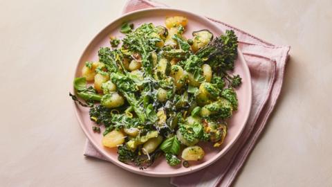 A pink plate fulled with crispy gnocchi and broccoli on a pink cloth 