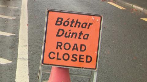 An orange road closed sign written in English and 'Bóther Dúnta' in Irish is placed in the middle of the road.