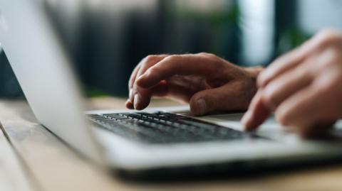 A partially blurred photo of a pair of hands typing on a grey laptop