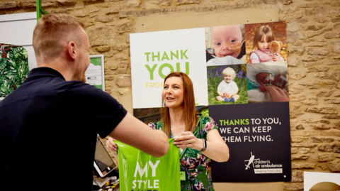 A female volunteer passes a man a green shopping bag from behind a till. 