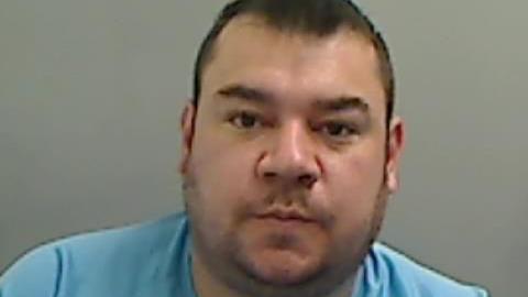 Mugshot of Madden. He has a large round face with faint stubble and short dark hair.