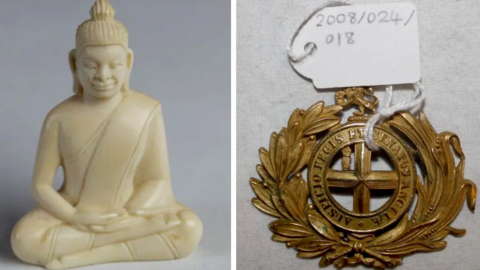 A carved ivory buddha with robes in a cross-legged position. It sits next to a circular belt buckle with a laurel motif with the words "Auspicio Regis et Senatus Angliae".