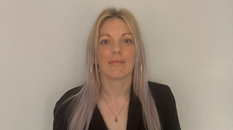 Woman with blonde and purple dyed hair looking directly at the camera against a white wall