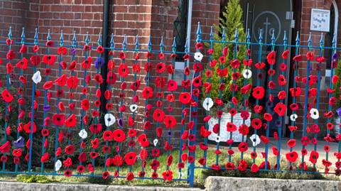 Crocheted poppies are attached to a metal gate outside a church.
