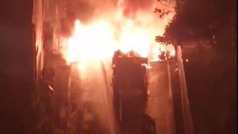 A truck on fire, with a firefighter spraying water over it.