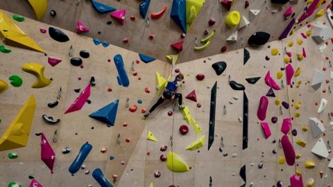 A climber, Connie Bridgens, is seen on a large indoor climbing wall with multicoloured grips