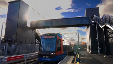 A red and blue Supertram is driving on the tracks under a metal pedestrian bridge
