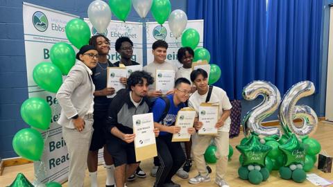 Students pose holding envelopes standing in front of a poster.