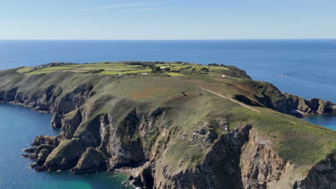 A birds eye view of Sark. There is a dirt path and lots of green fields. You can see the edges of the Island and surrounding sea